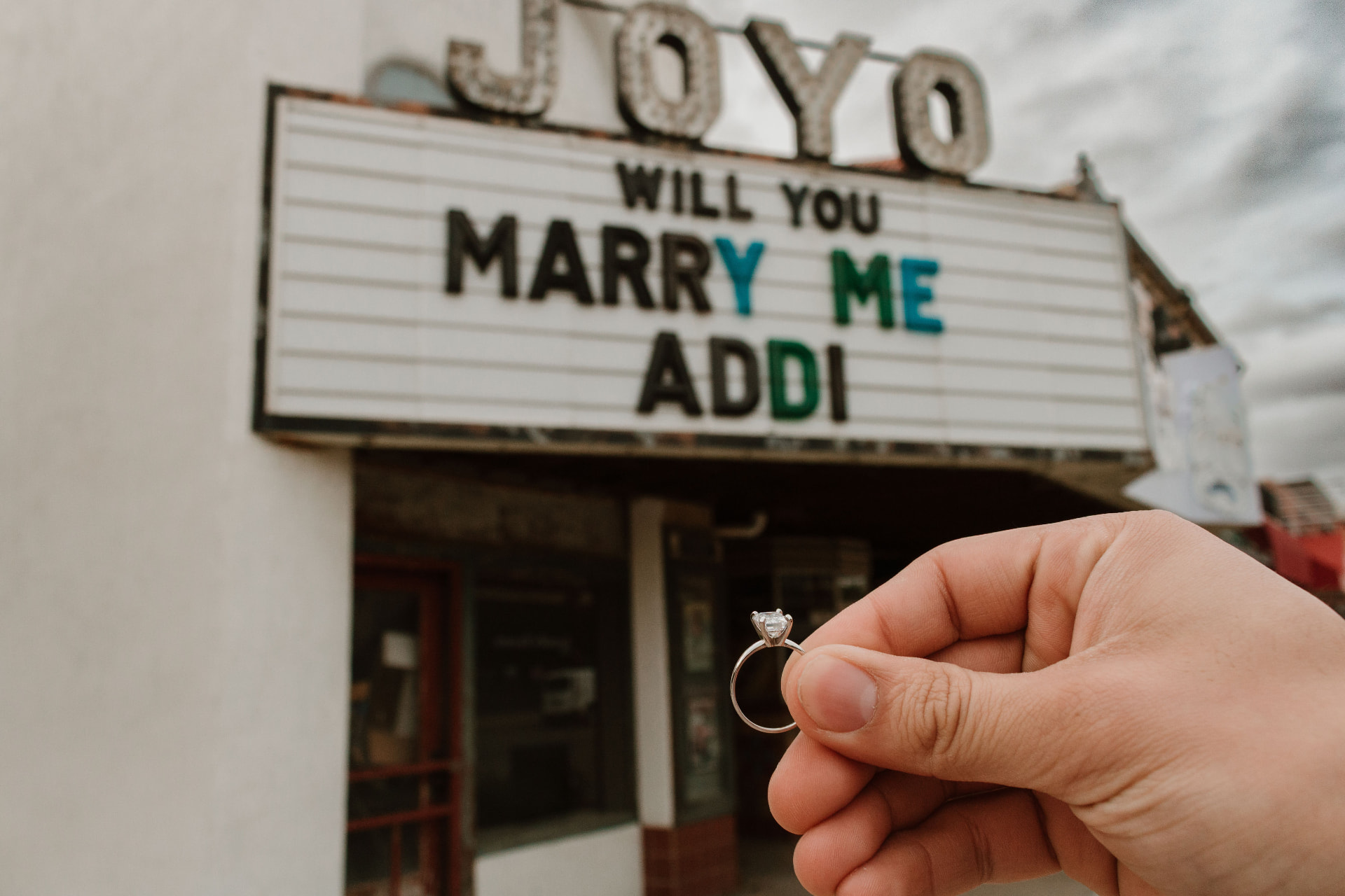 Geo holding up the engagement ring in front of the Joyo marquee